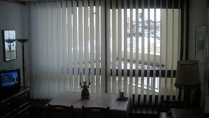 Una habitación tenuemente iluminada con una mesa, sillas, un televisor y una ventana con persianas.