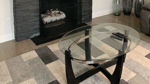 Een woonkamer met een flatscreen televisie boven een open haard, een glazen salontafel en drie vazen op een bijzettafeltje.