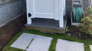 Een witte poort met een deur, een waterslanghouder en een kleine trap naar een houten terras.