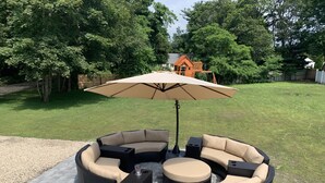 Een rond zitgedeelte buiten met een grote parasol, omgeven door een geplaveid terras.