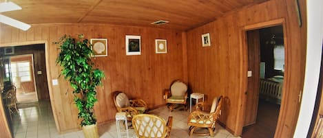 A wooden interior with wicker furniture, a potted plant, and framed pictures on the wall.