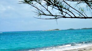 A beach with clear turquoise water, a distant island, and sparse vegetation. - Nice Wooden House, a few steps from the beach - sleeps 6 - Strategic location (Green Turttle)