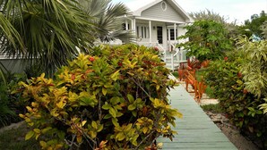 A house with a porch, surrounded by various plants and a wooden pathway. - Nice Wooden House, a few steps from the beach - sleeps 6 - Strategic location (Green Turttle)