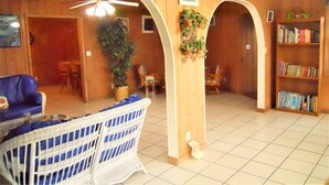 A cozy living room with wooden walls, a ceiling fan, a bookshelf, and a blue chair. - Nice Wooden House, a few steps from the beach - sleeps 6 - Strategic location (Green Turttle)