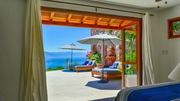 A bedroom with a bed, a view of the sea, and two lounge chairs with umbrellas. - Luxury 3-bed Villa,Spectacular Views, Saline pool & Staff   (Puerto Vallarta)