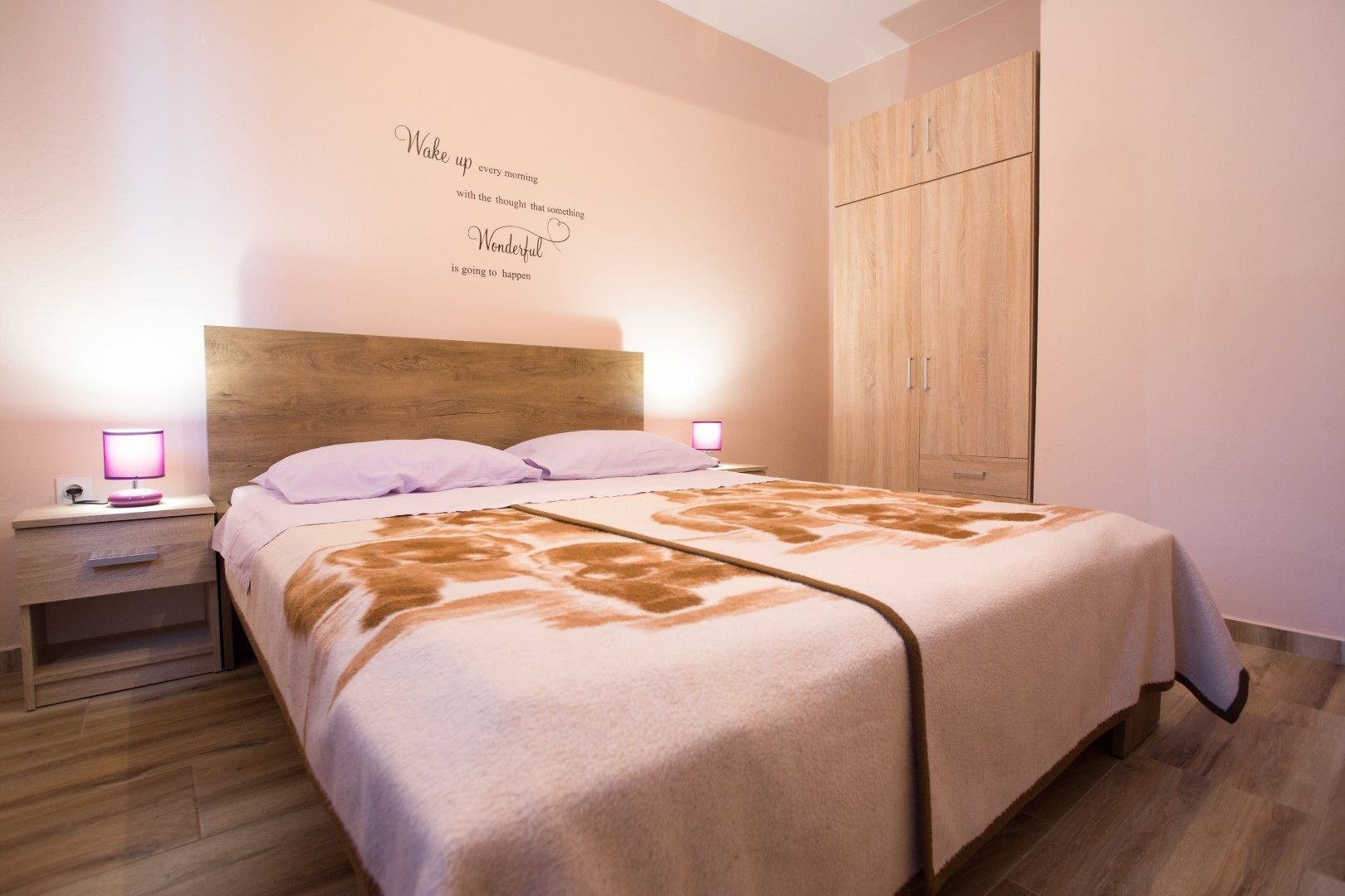 A bedroom with a wooden headboard, a bed with a patterned blanket, a nightstand with a lamp, and a wardrobe.
