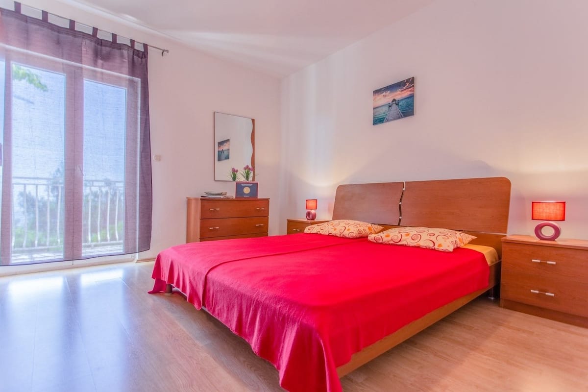 Een slaapkamer met een groot bed, houten nachtkastjes, een kast en een schuifpui naar een balkon.