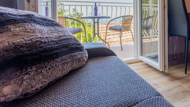 Une pièce comprenant un canapé, une petite table et des chaises, avec un balcon visible à travers la porte vitrée.
