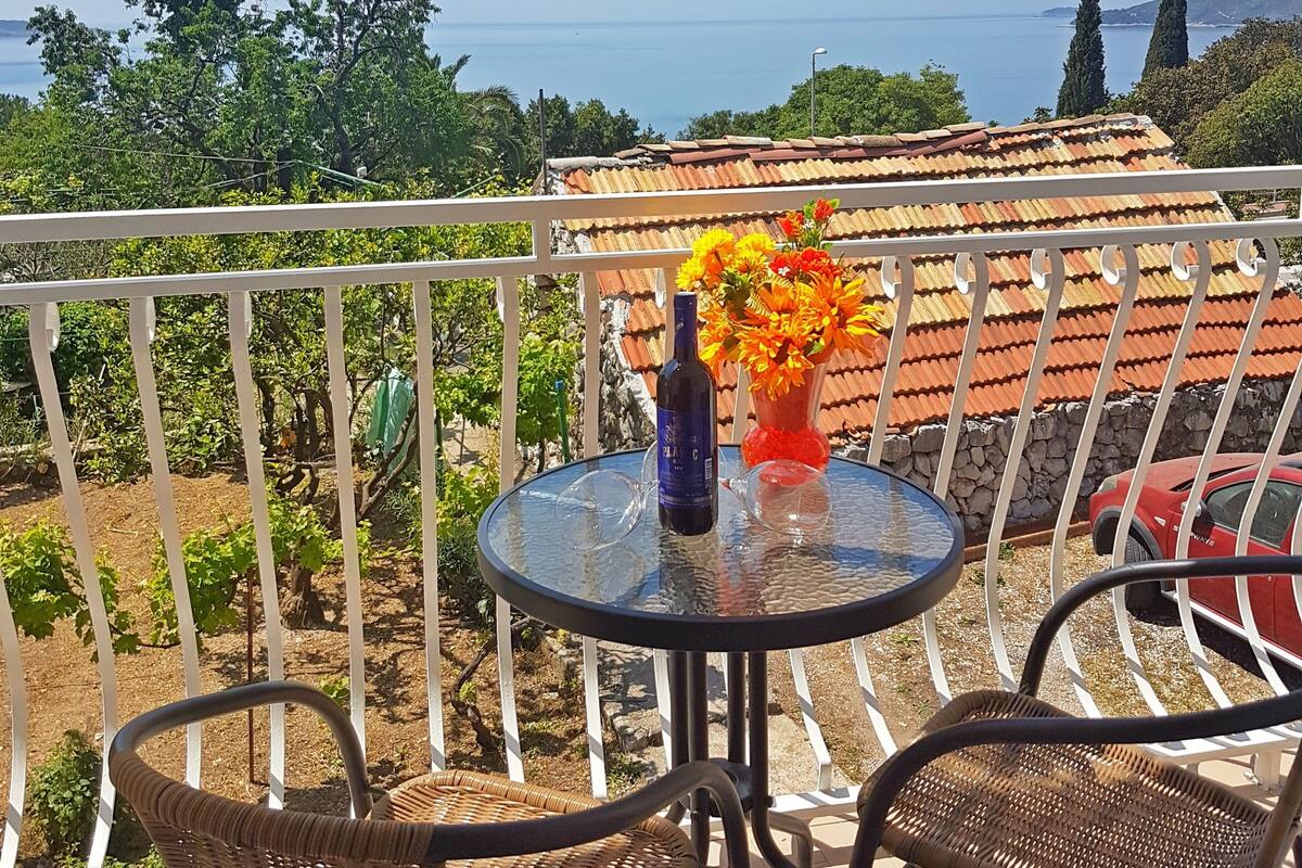 Een balkon met een tafel en stoelen, met uitzicht op de kust onder een heldere lucht.