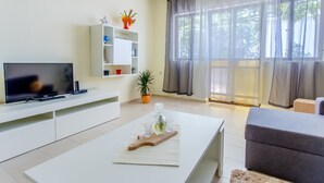 Un salon moderne avec un téléviseur à écran plat, une étagère blanche, une plante en pot et un canapé gris.