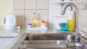 Une cuisine équipée d’un évier en acier inoxydable, d’une bouilloire et de divers produits de nettoyage disposés sur le plan de travail.