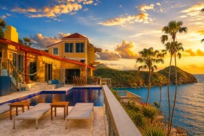 A beachfront property with a pool, outdoor seating, and a view of the ocean at sunset. - Cliffside Retreat | Infinity Pool, Yoga Deck, 9 BR (St. Thomas)
