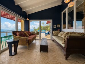 A room with a view of the sea, furnished with a sofa, a bench, and a table.