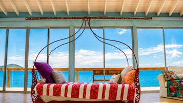 A room with a swing chair, large windows, and a view of the sea.