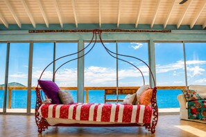 A room with a swing chair, large windows, and a view of the sea.