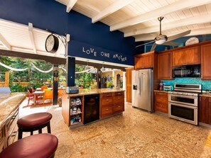 A modern kitchen with a central island, wooden cabinets, stainless steel appliances, and a ceiling fan. - Cliffside Retreat | Infinity Pool, Yoga Deck, 9 BR (St. Thomas)