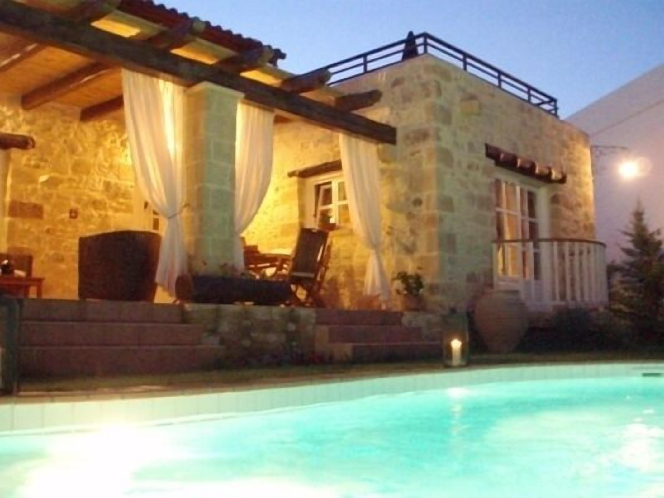 A stone building with a pool, featuring a covered patio area with chairs and a table.
