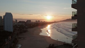 A beach with a sunset, a sandy shore, and buildings in the background. - Beautifully decorated apartment! Maulf Hill - Ocean View! 150m2 (Guarujá)