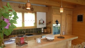 Cocina de cabaña de madera con encimera de madera, luces de cobre colgantes, ventana con cortinas y un refrigerador.