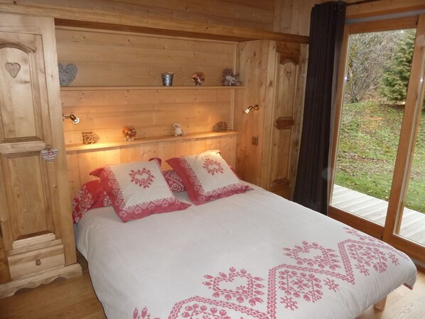Un dormitorio de cabaña de madera con cama, almohadas, estantes con adornos y vistas al exterior.