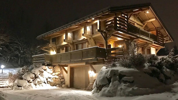 Un chalet de madera grande y de varios pisos con balcón y cimientos de piedra, rodeado de nieve.