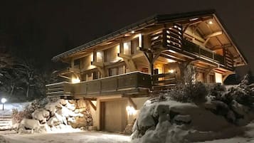 Un grand chalet en bois à plusieurs étages, doté d’un balcon et de fondations en pierre, entouré de neige.