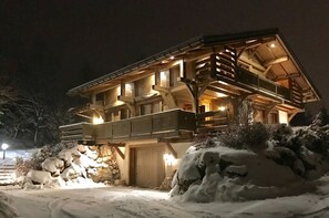 Un chalet de madera grande y de varios pisos con balcón y cimientos de piedra, rodeado de nieve.