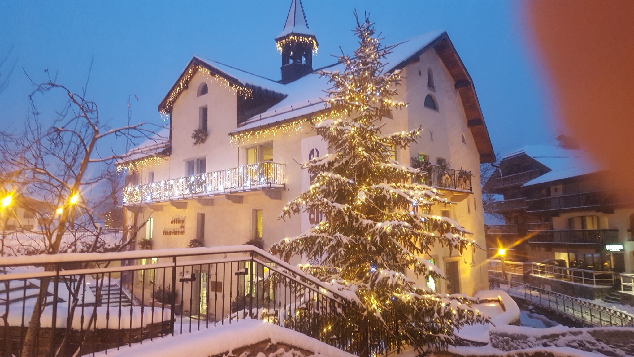 Un hôtel doté d’un balcon, dont le sol est recouvert de neige, et qui arbore un sapin de Noël illuminé.