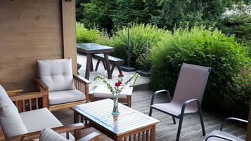 Une terrasse en bois, agréée de meubles d’extérieur, notamment des chaises et une table, et entourée d’une végétation luxuriante.