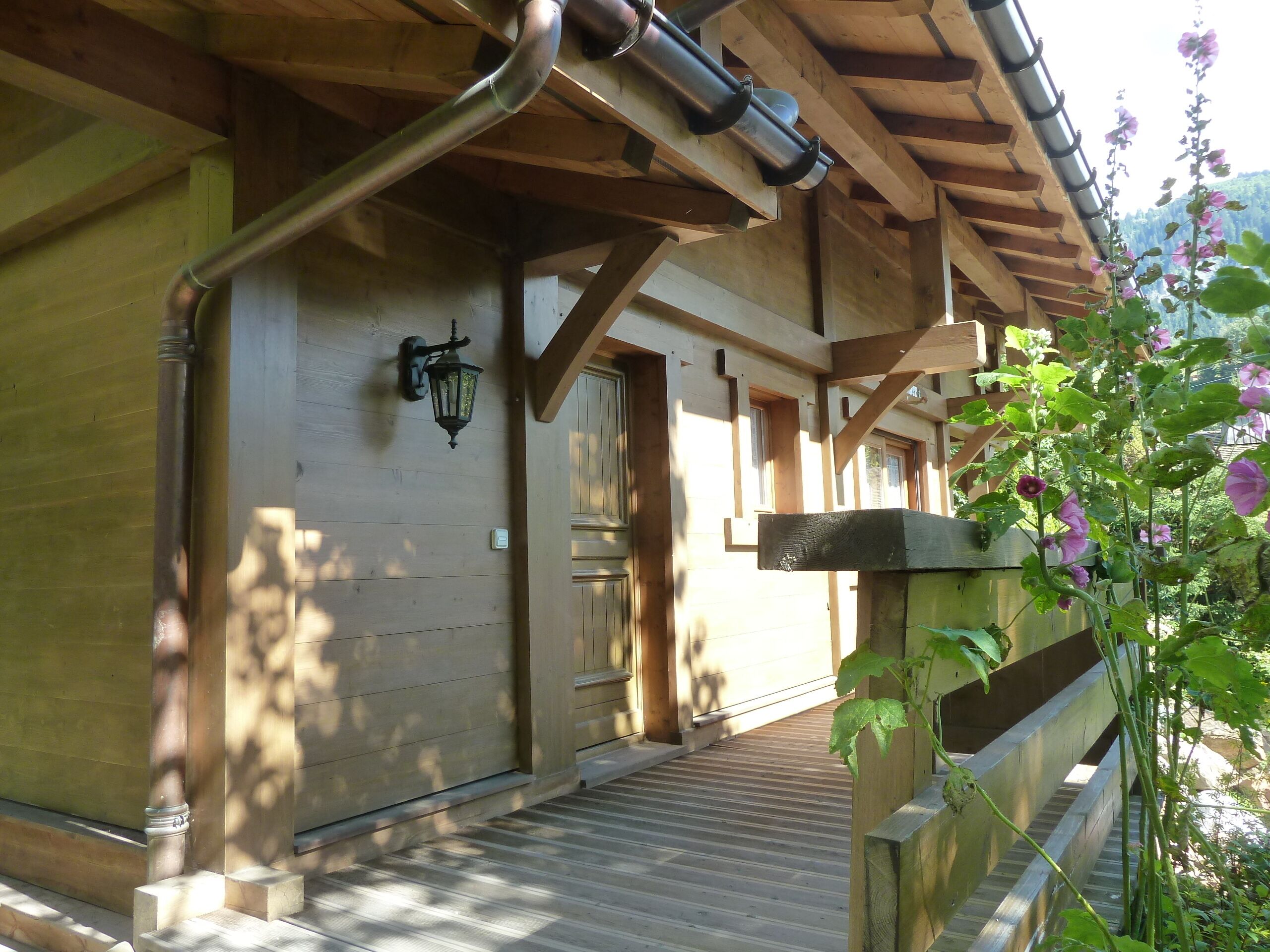 Un bâtiment en bois doté d’un porche couvert, d’un luminaire fixé au mur et d’un escalier en bois menant à une porte.