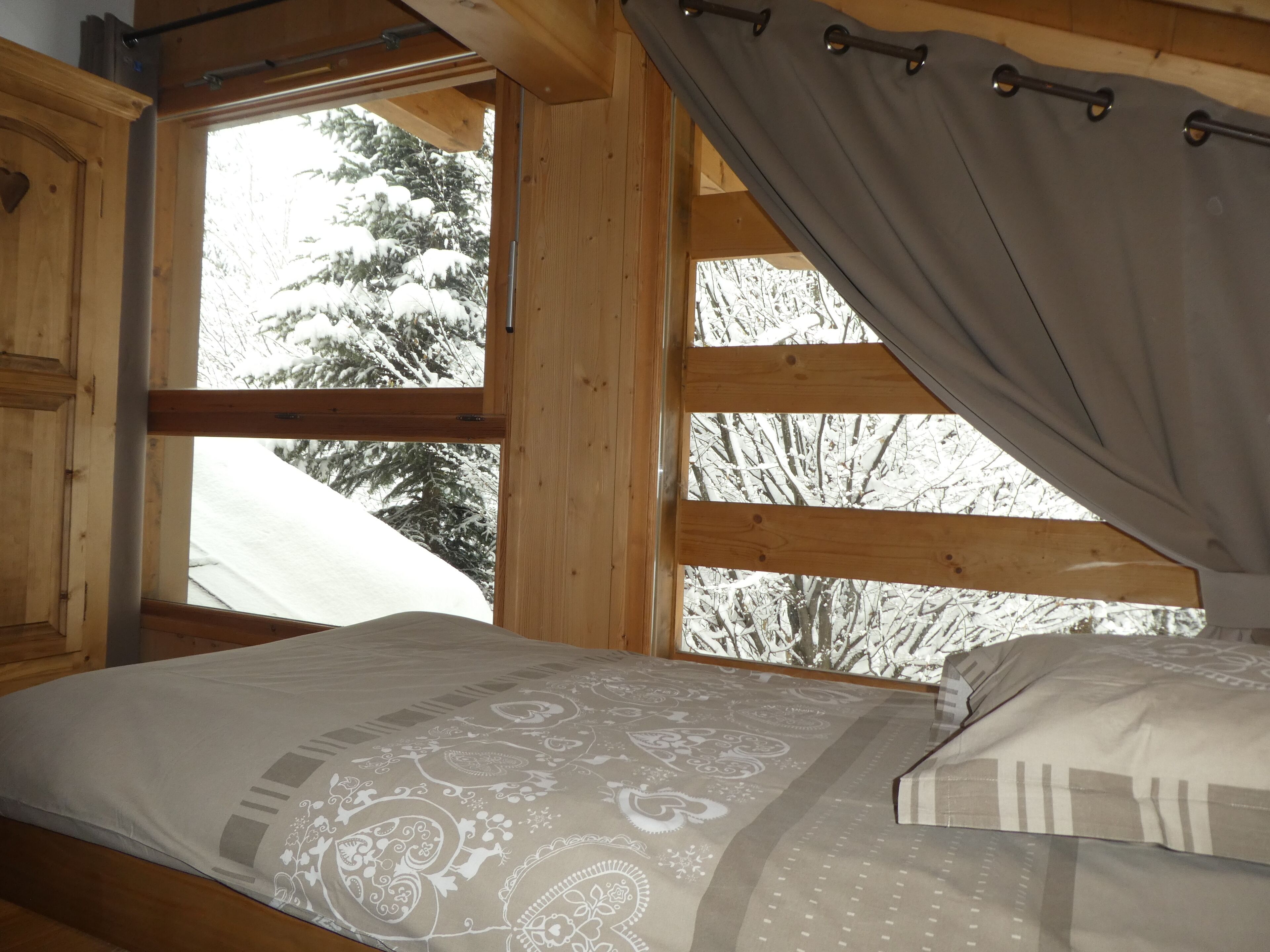 Une chambre dans une cabane en bois, avec un lit, une fenêtre avec des rideaux et une vue sur des arbres couverts de neige.