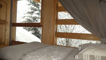 Une chambre dans une cabane en bois, avec un lit, une fenêtre avec des rideaux et une vue sur des arbres couverts de neige.