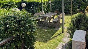Un espace jardin agrémenté d’une table de pique-nique et de bancs, entouré de haies bien entretenues et sous un ciel dégagé.