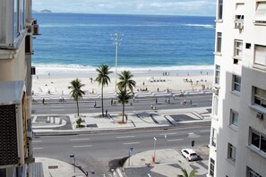 Blick auf einen Strand von einem Hochhaus aus, mit Palmen, einer Straße und einem klaren, blauen Himmel.