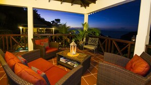 A covered outdoor seating area with wicker furniture, a coffee table, and a view of the ocean at dusk. - Upper Level apartment overlooking Marigot Bay (Marigot bay)
