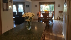 A dining area with a wooden table and chairs, a vase with flowers, and a view of the outdoors through large windows. - All Star Acres 2 Miles To Park
5 BR,3 baths
 Dates align with Dreams Park ONLY! (Milford)