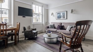 Ein Wohnzimmer mit einer Couch, Sesseln, einem Couchtisch und einem Fernseher.