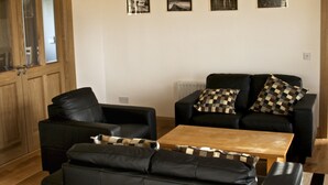 A living room with a black sofa, a wooden coffee table, and a wooden door. - Beautiful Holiday Cottage, Dunfanaghy, Donegal (Dunfanaghy)