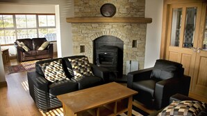 A living room with a stone fireplace, leather sofas, a wooden coffee table, and a striped rug. - Beautiful Holiday Cottage, Dunfanaghy, Donegal (Dunfanaghy)