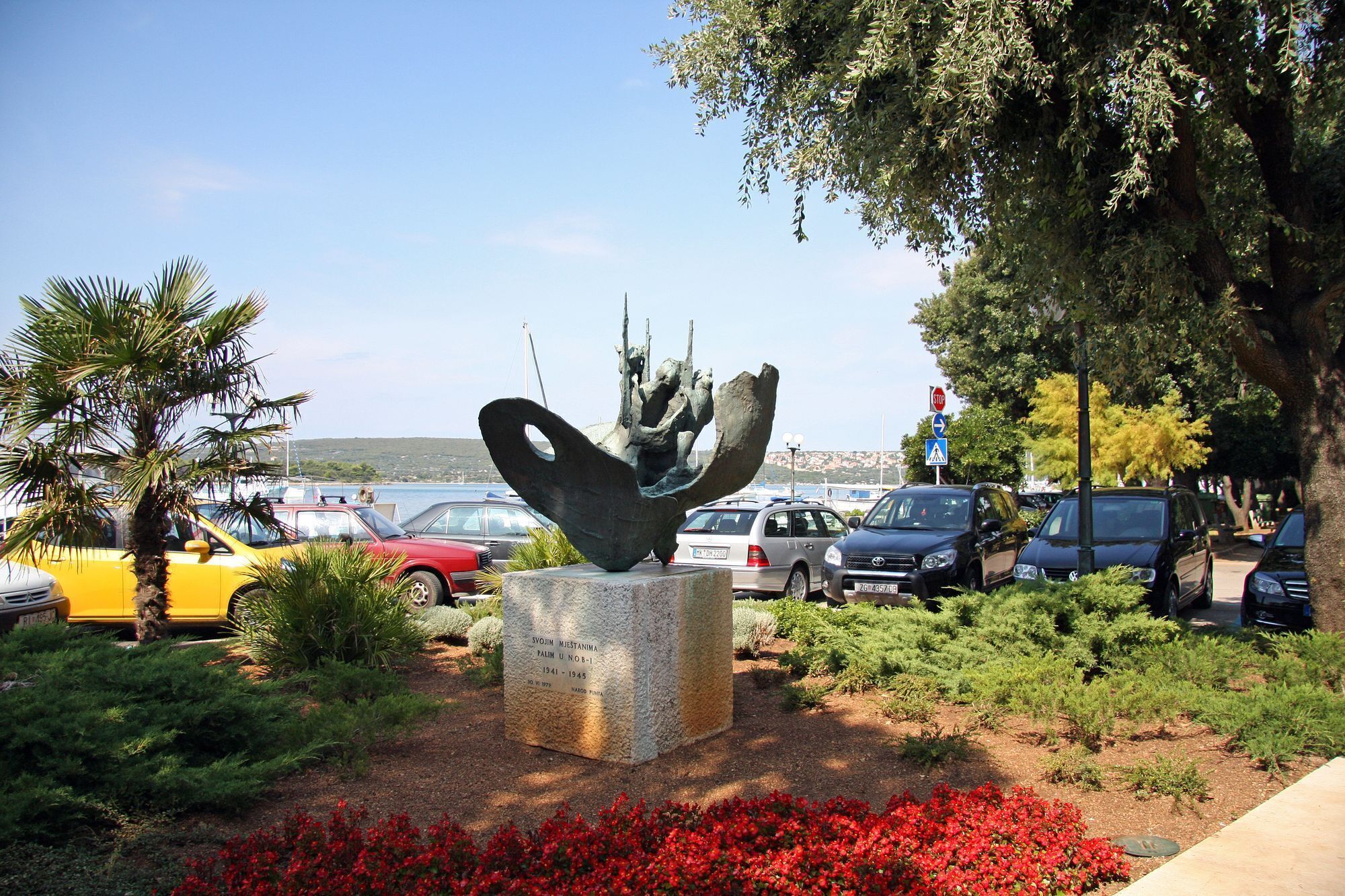 Een sculptuur in een aangelegd gebied, met geparkeerde auto's en een heldere lucht.
