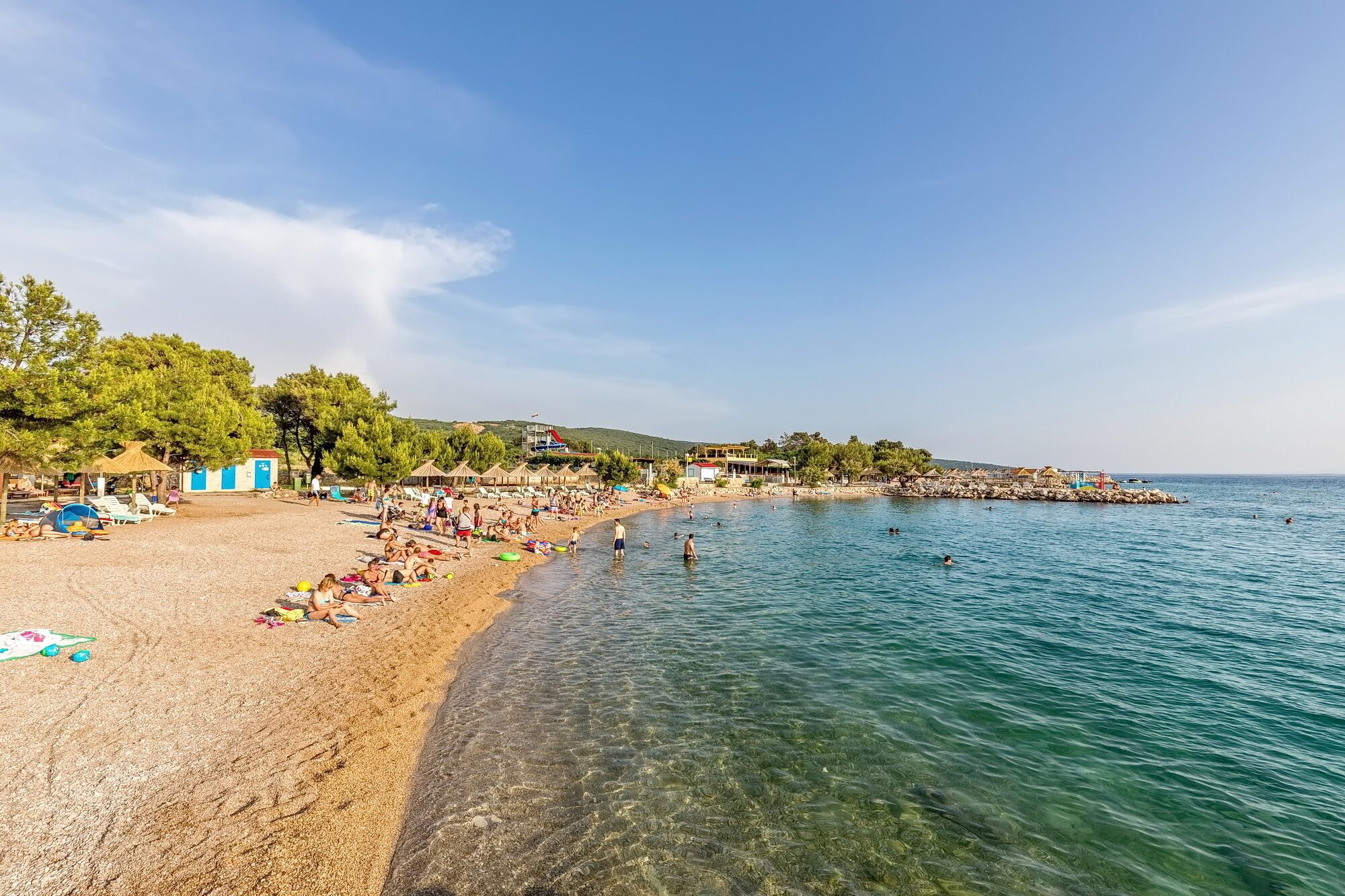 Une plage avec une eau claire, des parasols et des gens.