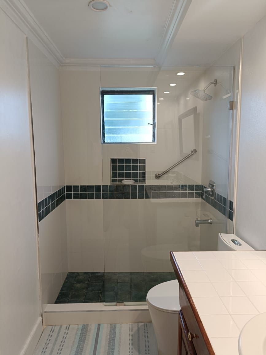 A walk-in shower with a small window, a handrail, and a tiled floor.