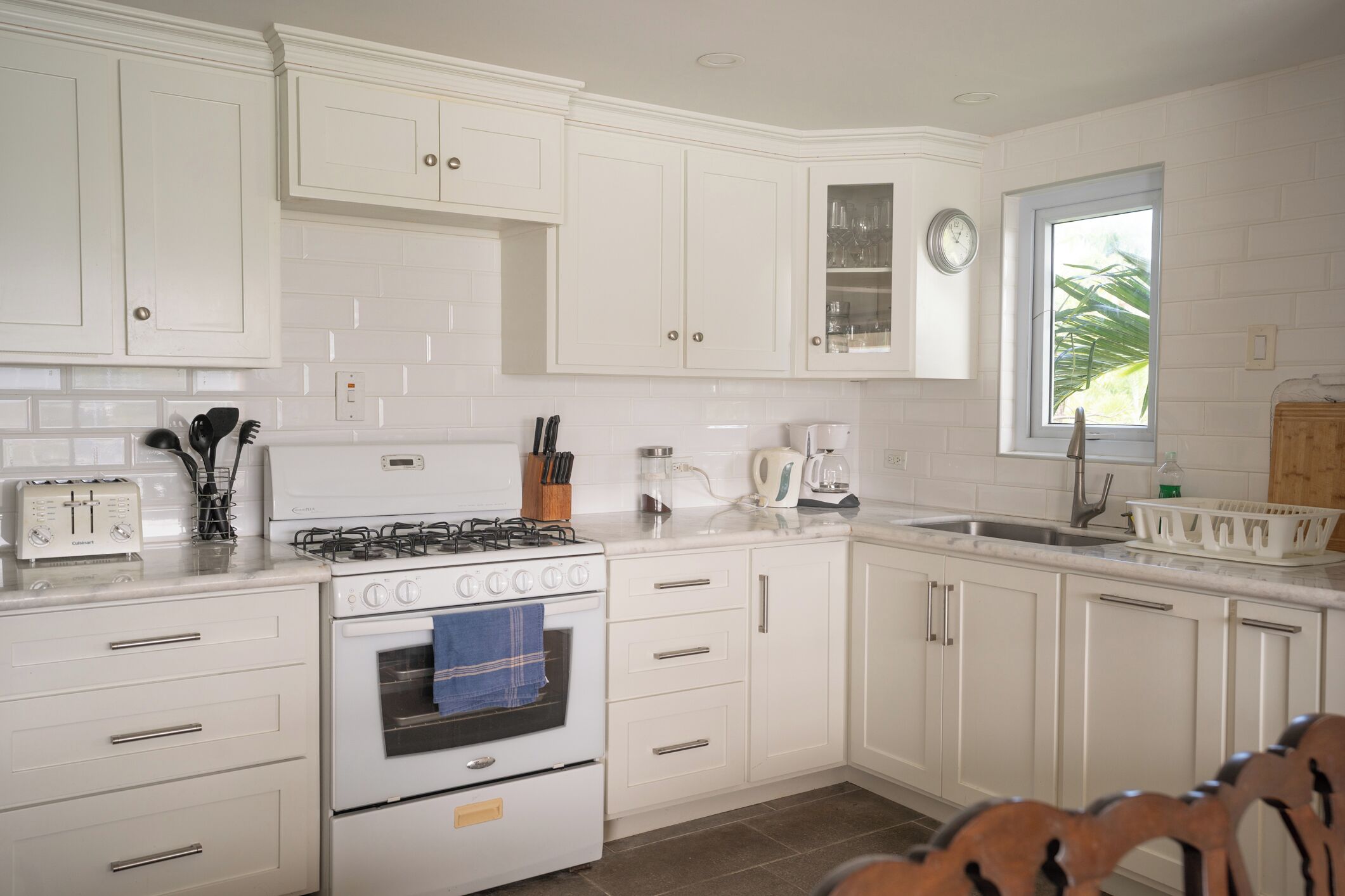 A kitchen with white cabinetry, a stove, a coffee maker, and a window with a view.