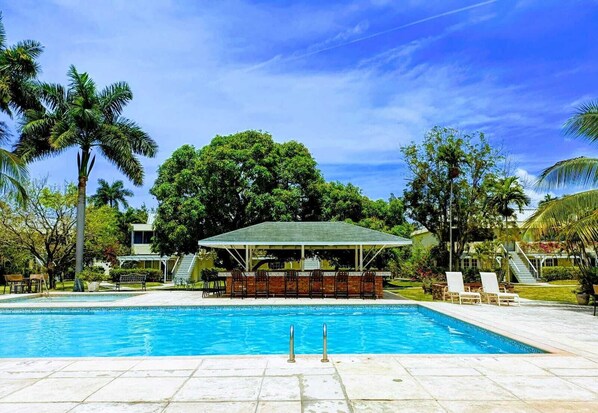 A swimming pool with a covered bar area, surrounded by palm trees and a clear sky.