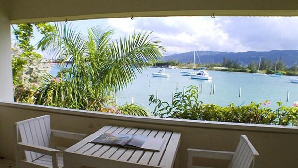 Ein Balkon mit Tisch und Stühlen mit Blick auf eine Marina, in der Boote liegen, vor einer Bergkulisse.