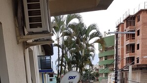 Un balcón con una antena parabólica, un tendedero y vistas a palmeras y edificios al fondo.