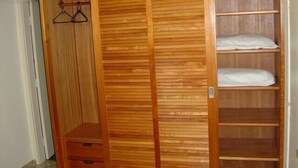 Un armario de madera con múltiples estantes y cajones, una barra para colgar y una puerta con tirador.