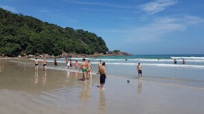A beach with people walking along the shore, a rocky outcrop in the background, and the ocean in the distance. - 4 bedroom apartment in ubatuba close to the beach (Ubatuba)