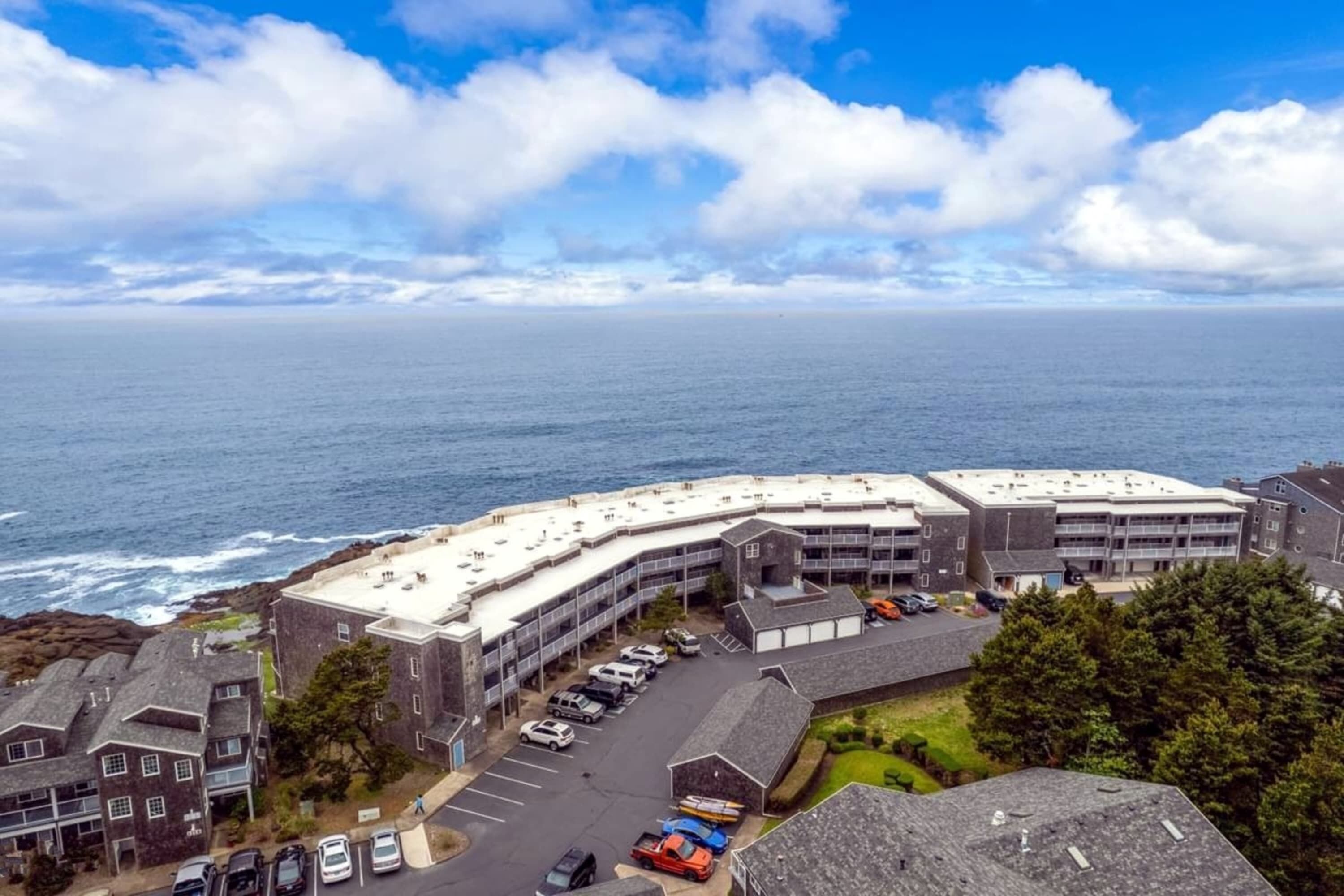 A coastal hotel with a parking lot, multiple buildings, and a view of the ocean.