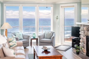 A living room with a view of the ocean, a fireplace, and a television.